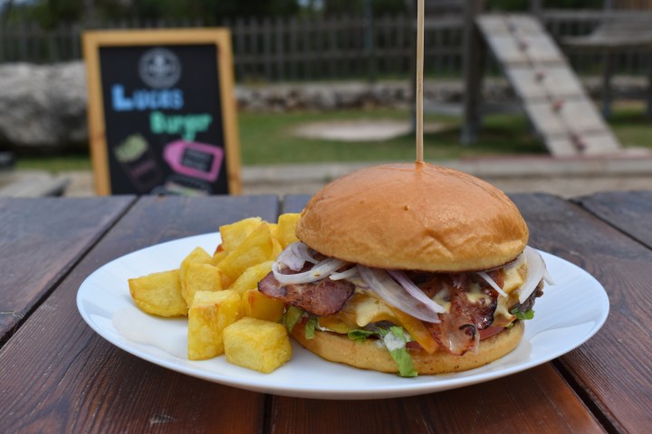 Burger and fries on a white plate outdoors with a chalkboard menu in the background.
