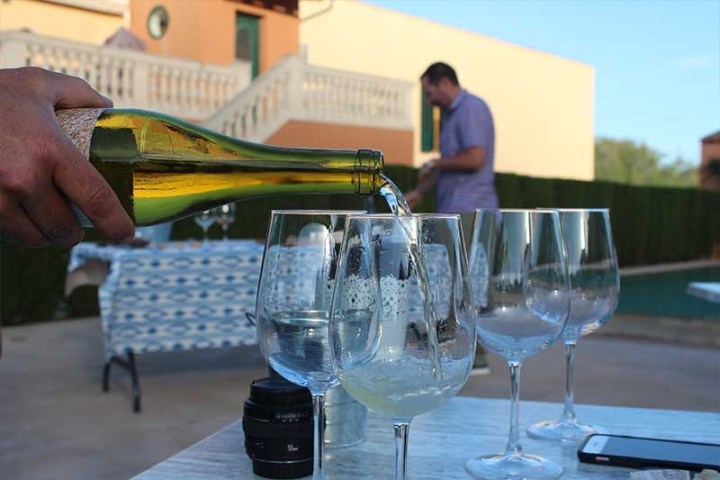 Person pouring white wine into glasses outdoors with a blurred background.